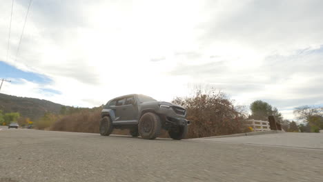 toma fpv de un coche todoterreno futurista conduciendo por una carretera rural bajo un cielo azul