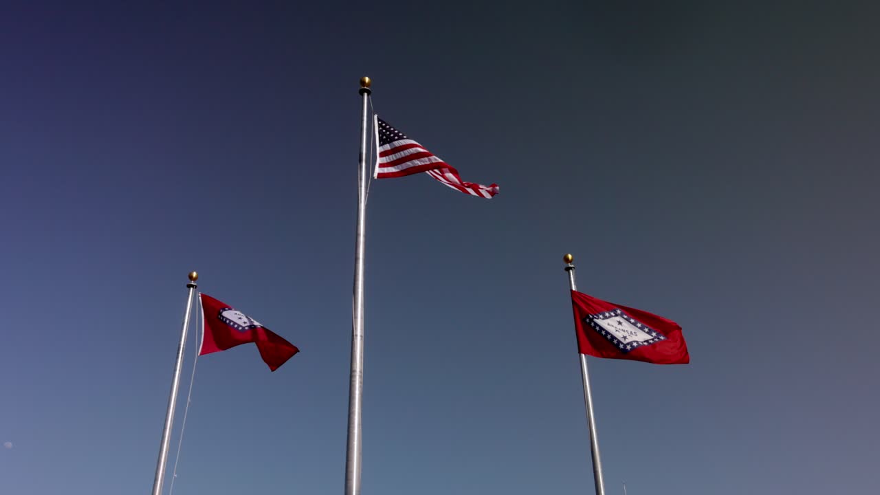 Arkansas state flags and American flag waving in the wind in slow motion