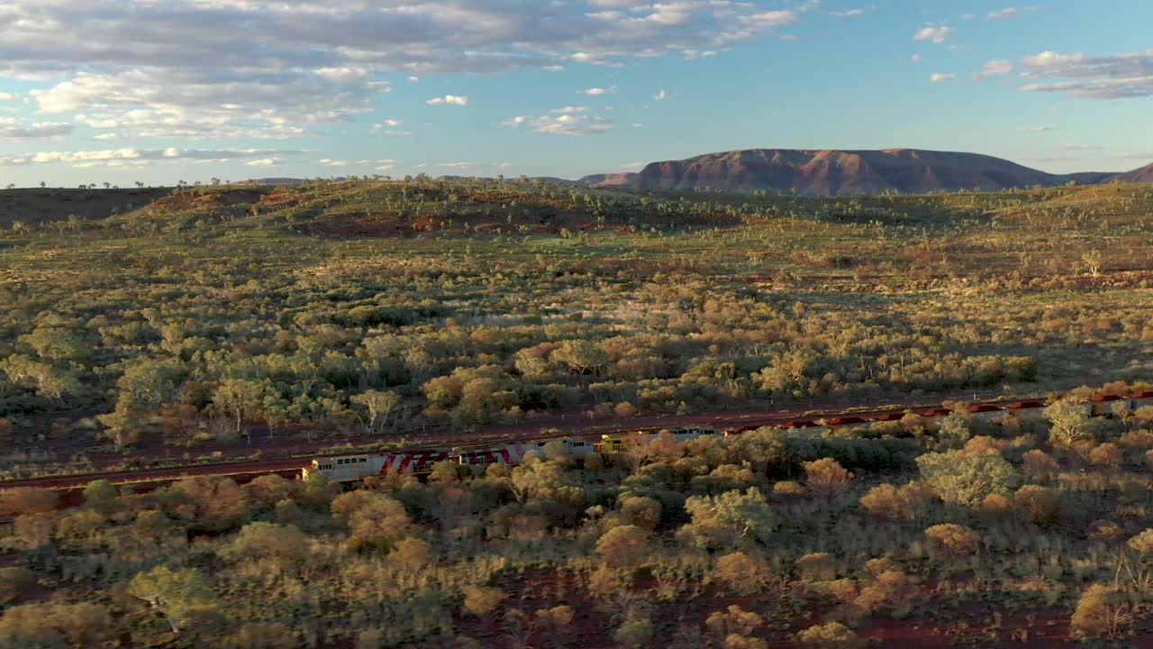 excelente toma aérea de un tren de carbón que pasa por arbustos y montañas en tom price, australia