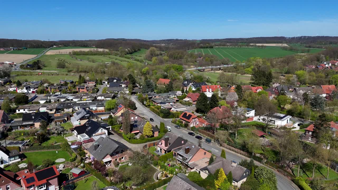 Modern two-story homes in quiet american village in spring. Aerial forward wide shot. Traffic on interstate road in background. Farm fields on mountains in usa.