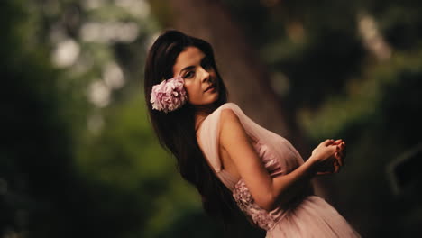 disparo giratorio de una joven bonita con cabello negro grueso con una flor en él y un vestido rosa