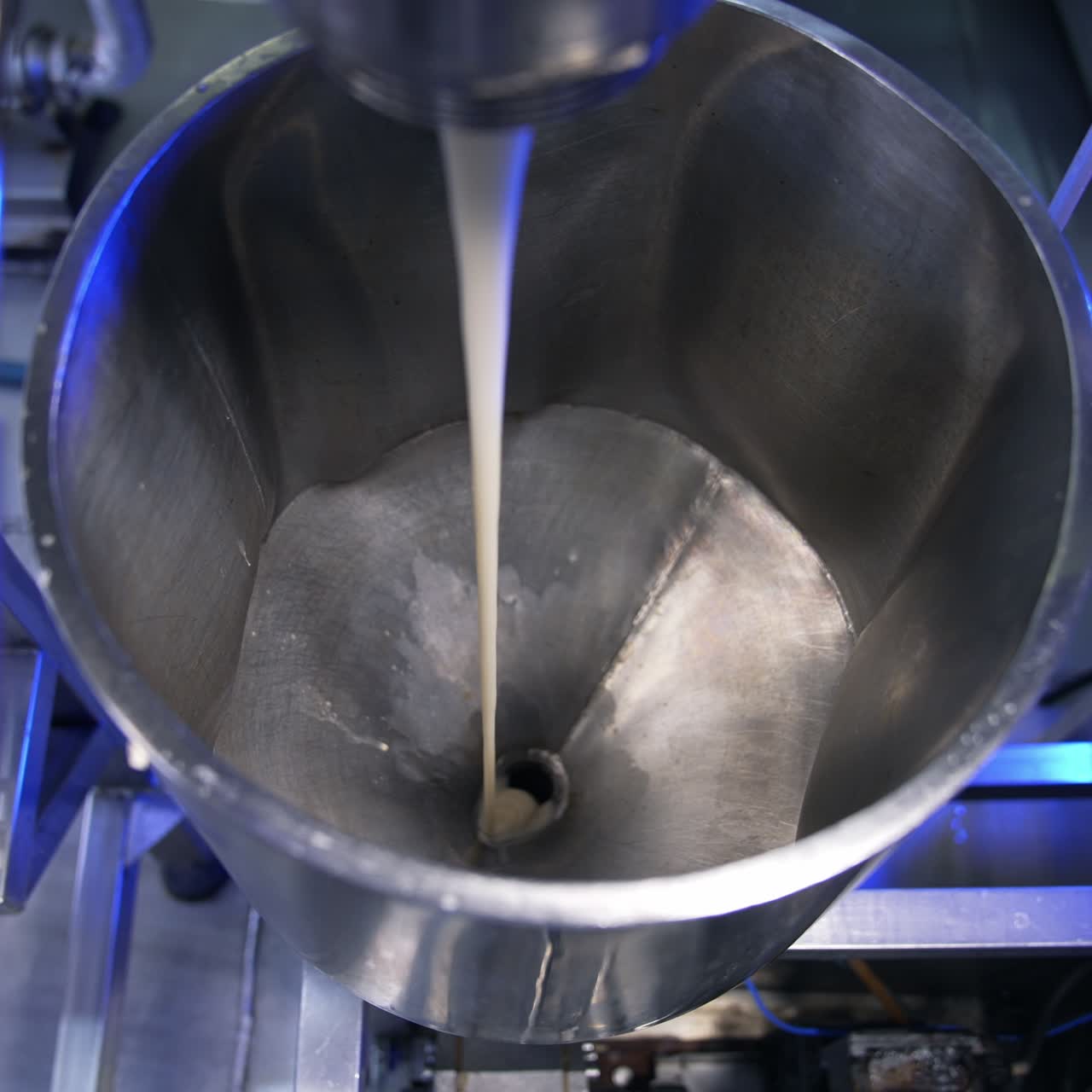 Condensed milk streaming from a tube into a metal container. Close up. Food factory automated line. View from above