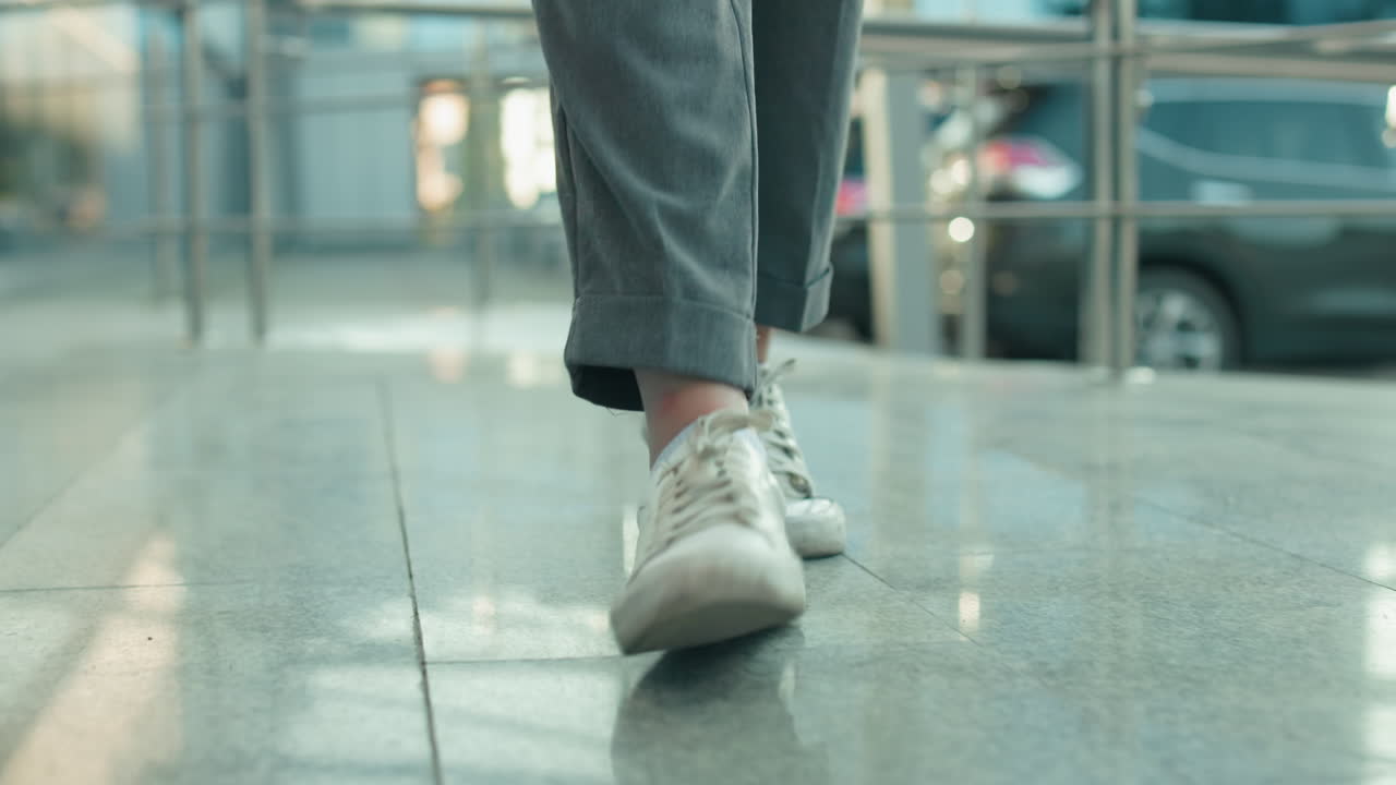 Leg view of individual in white sneakers and gray trousers dancing energetically on sleek polished tile surface with metal railings and parked cars in background