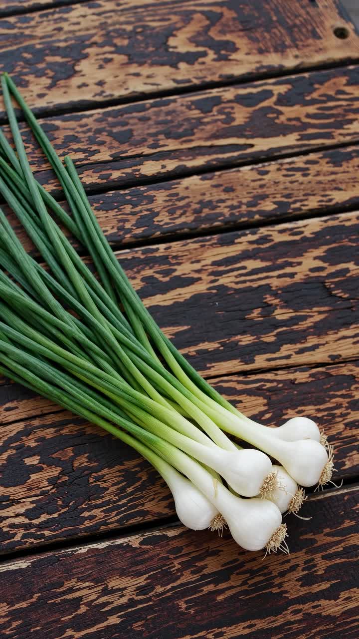 Top-down video shot of fresh green onions on a rustic wooden table, highlighting their vibrant