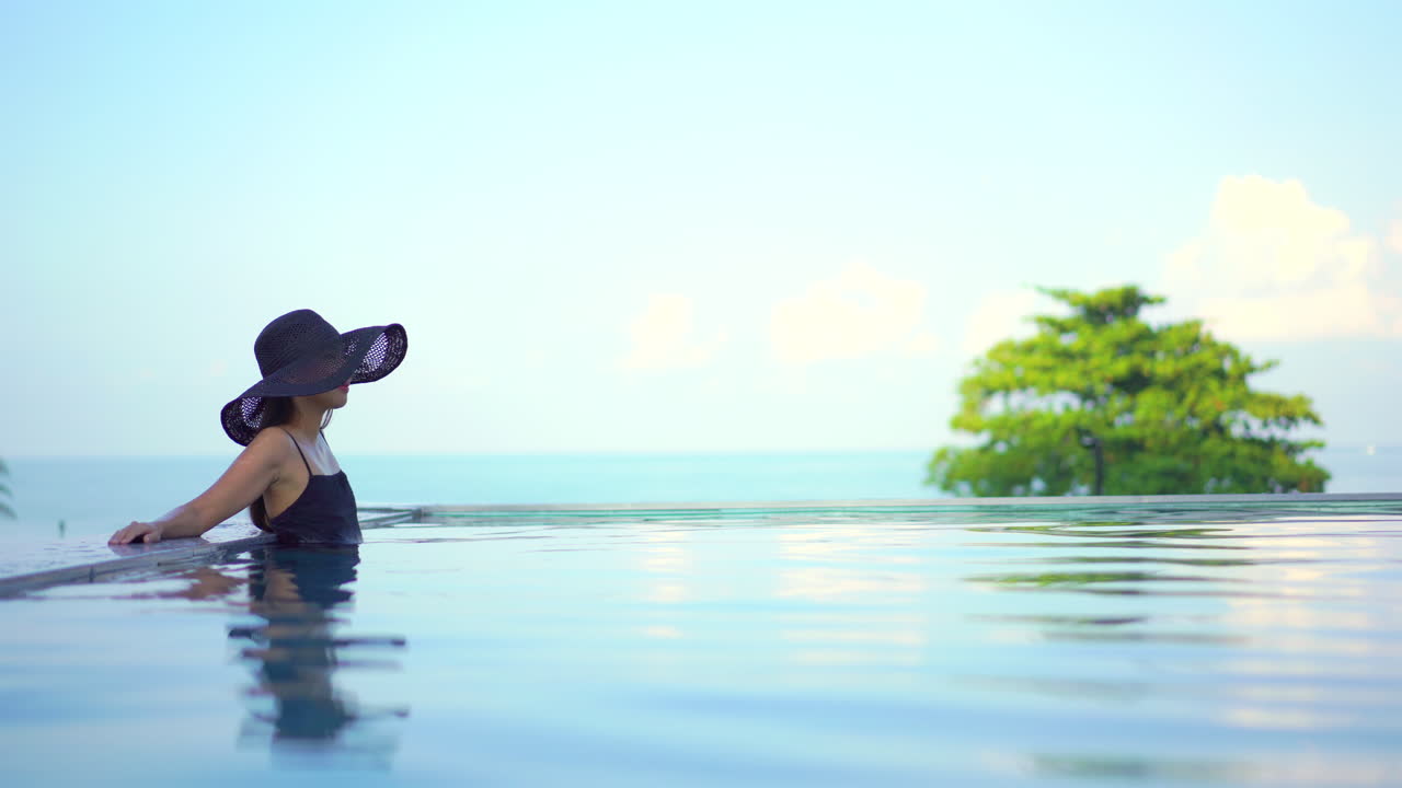 Schöne, elegante Frau in modischer Bademode in einem Infinity-Pool, unscharfer Hintergrund, weiches Licht.