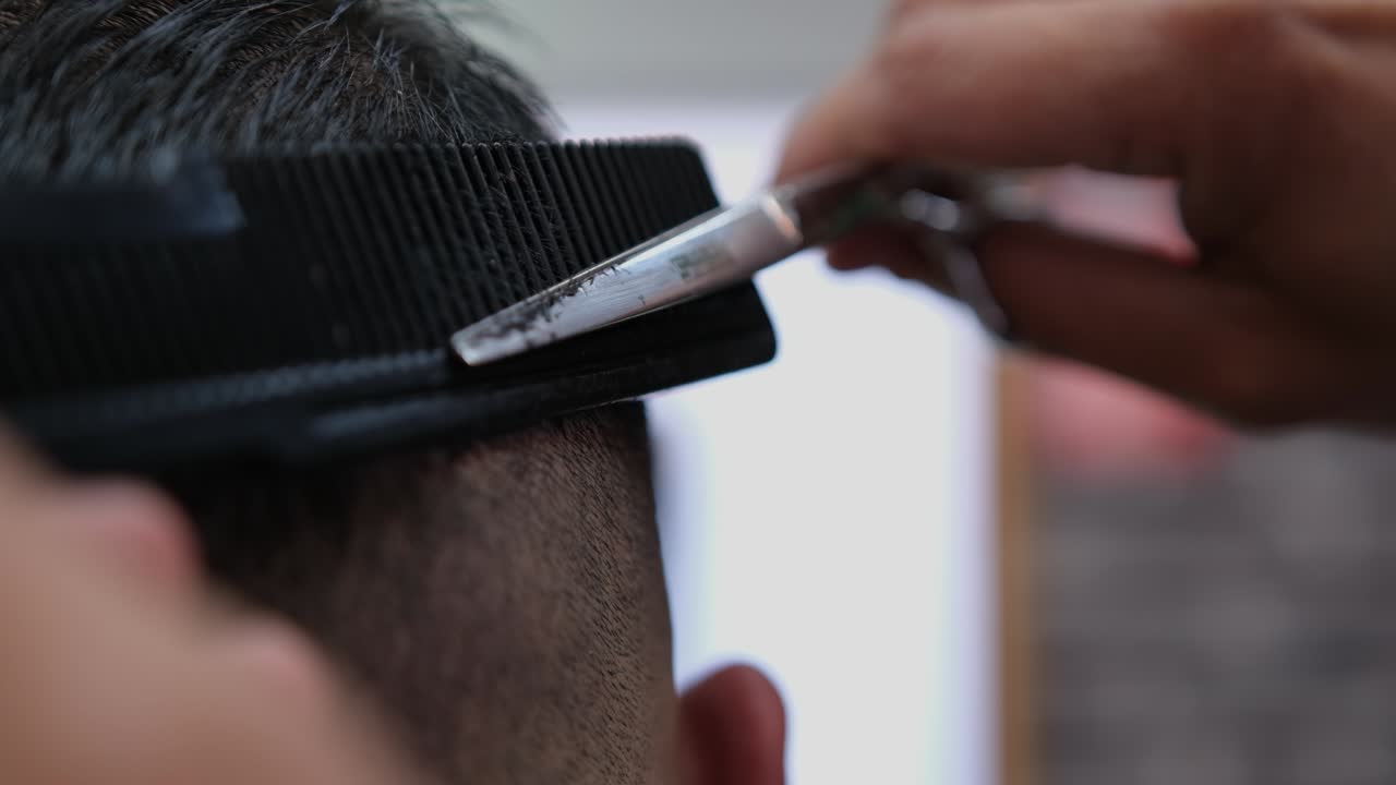 primer plano extremo de un peluquero que termina de difuminar el corte de pelo de un cliente masculino.