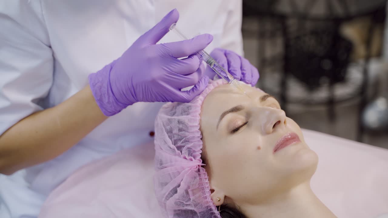 A beautiful woman is on the procedure of facial rejuvenation. Beautician makes mesotherapy of the forehead area. Beauty injections