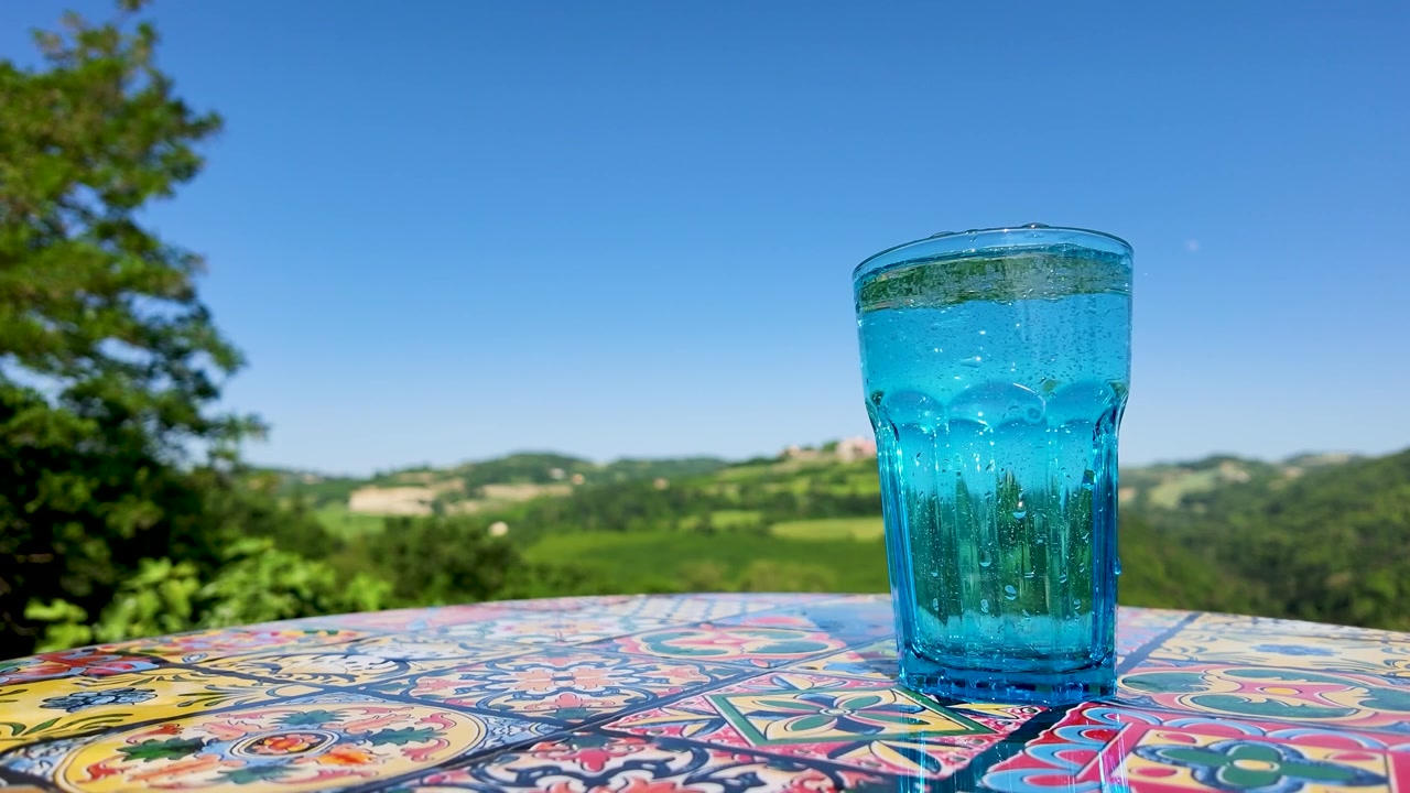 Carbonated water bubbles inside a blue glass on a patterned table with rolling green hills.