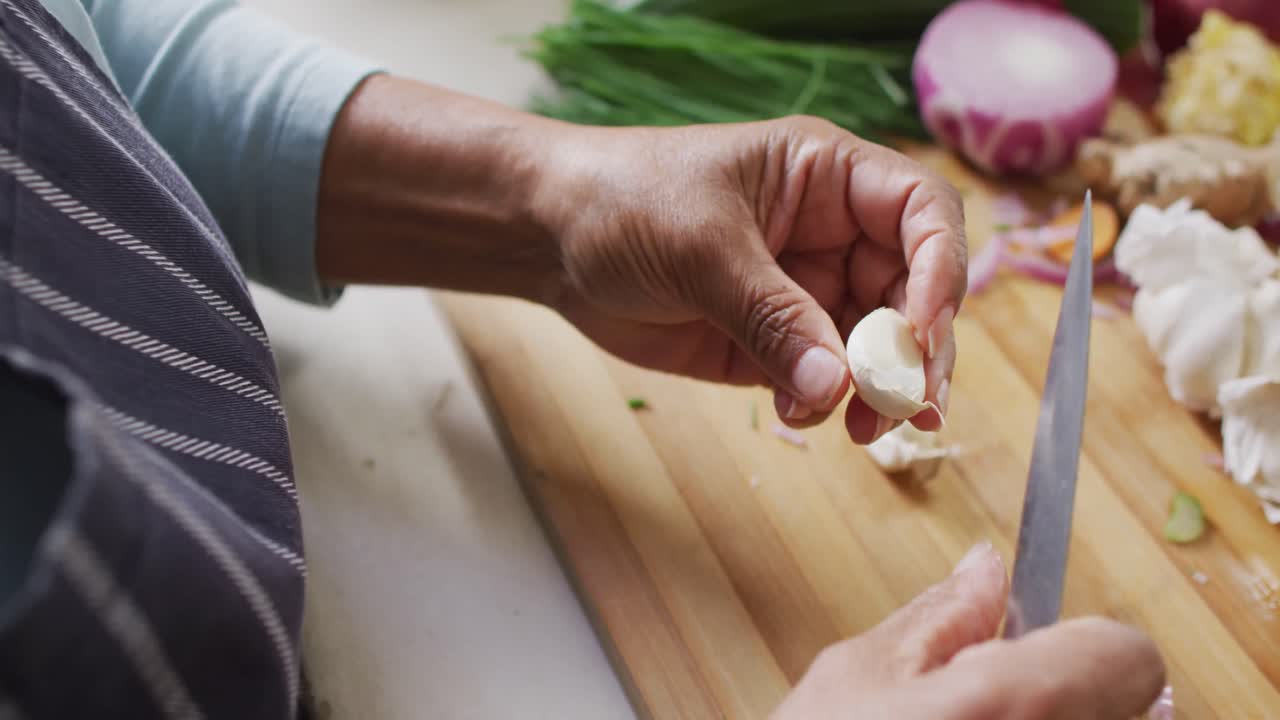 Mid section of asian senior woman removing the skin of garlic in the kitchen at home