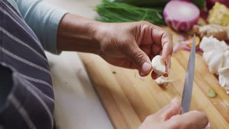 Mid-section-of-asian-senior-woman-removing-the-skin-of-garlic-in-the-kitchen-at-home