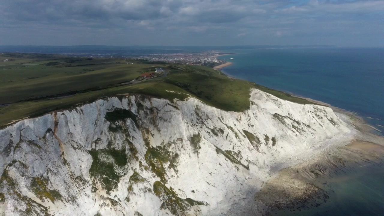 Widok z drona na białe klify kredowe Beachy Head, rozciągające się wzdłuż kanału La Manche, z zielonym zboczem wzgórza, skalistym brzegiem i odległym Eastbourne, Anglia, Wielka Brytania