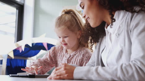 Eine-Kleinkindlehrerin-Arbeitet-Mit-Einem-Jungen-Weißen-Schulmädchen,-Das-Ein-Tablet-Benutzt,-Nahaufnahme,-Niedriger-Winkel