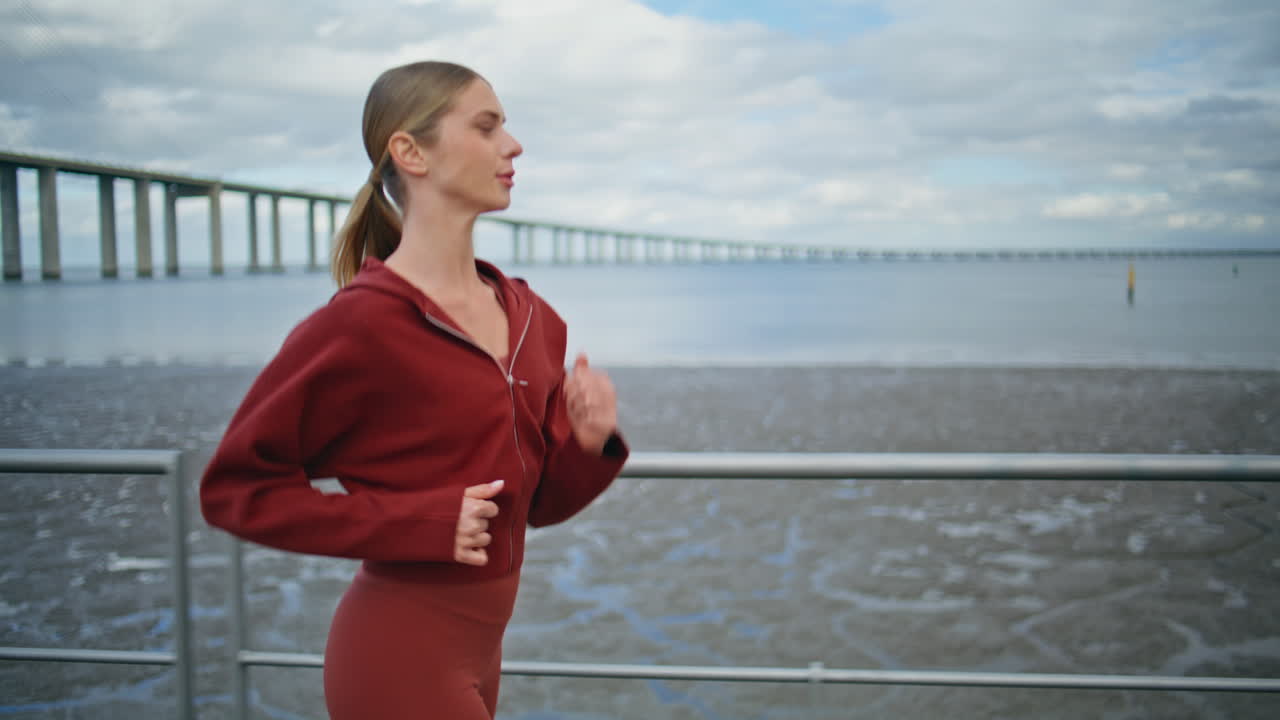 Attractive girl training cardio at city coast. Motivated athlete running morning