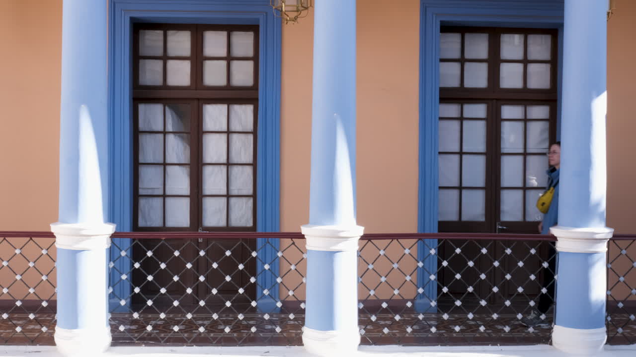 Traveler walks by blue colonial pillars at Museo Charcas in Sucre, Bolivia, exploring stunning architecture