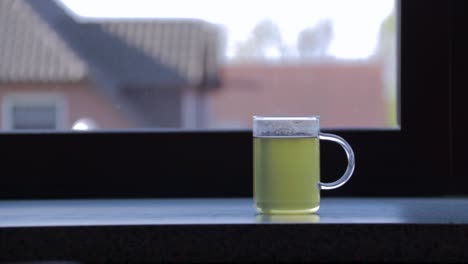 Side-view-of-hot-glass-cup-of-green-tea-in-front-of-window