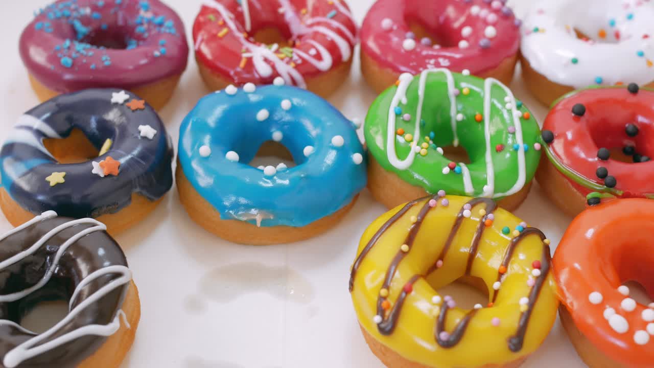 Soft fluffy donuts covered with multi-colored glaze and poured with dark white chocolate are laid out in three rows on the table. Hand gently take one of the donuts .. Sweets close-up. Junk food