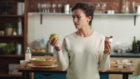 woman making choice between apple and cake in kitchen. girl choosing fruit diet.