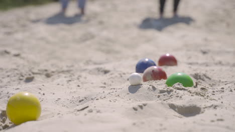 close-up view of colorful petanque balls on the sand on the beach, then a player throws another ball nearby