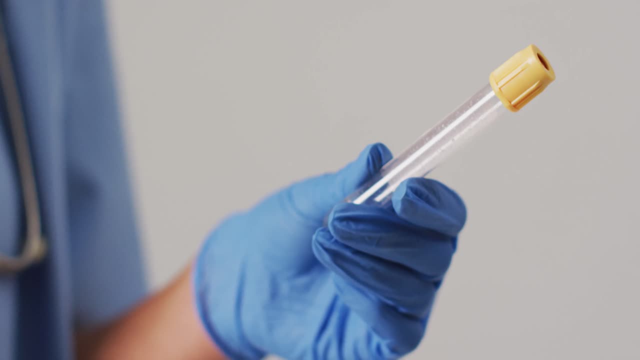 video de una doctora biracial sosteniendo un tubo de ensayo sobre un fondo azul