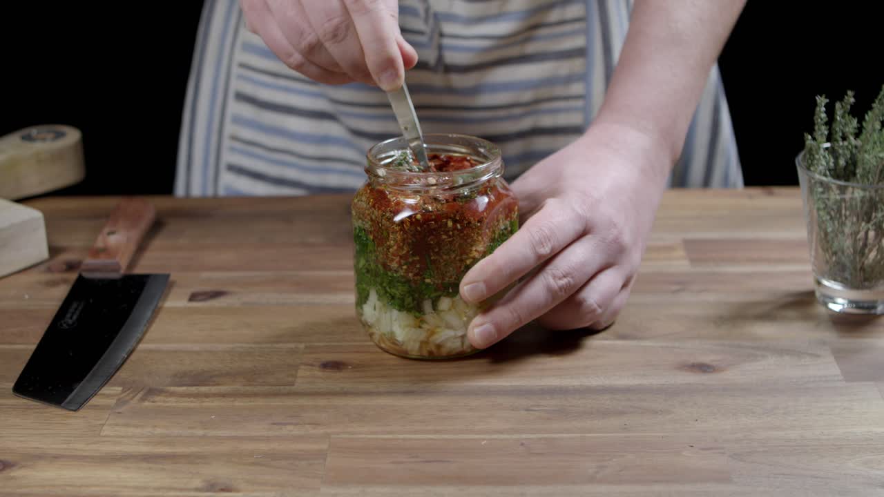 agitando delicadamente con una cuchara los ingredientes de la salsa chimichurri argentina en un frasco de vidrio