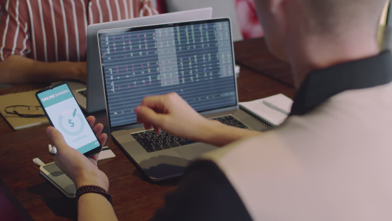 Trader Transferring Money to Bank Account Using Phone and Laptop