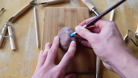 An-artist-sculpting-brown-modeling-clay-with-tools-and-brushes-to-make-a-face-mask-figurine-project-in-his-art-studio