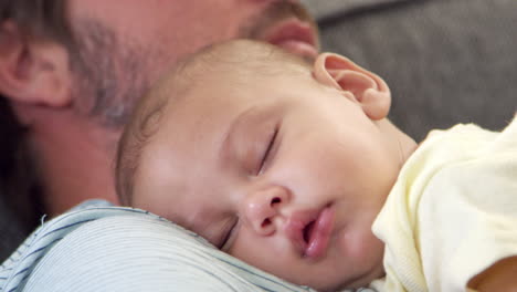 cerca del padre sentado en el sofá sosteniendo al hijo bebé durmiendo