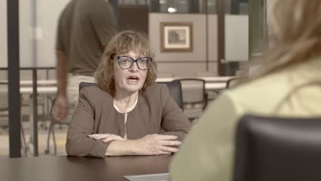 Senior Citizen woman talking to a young woman in an office setting with video dolly left to right