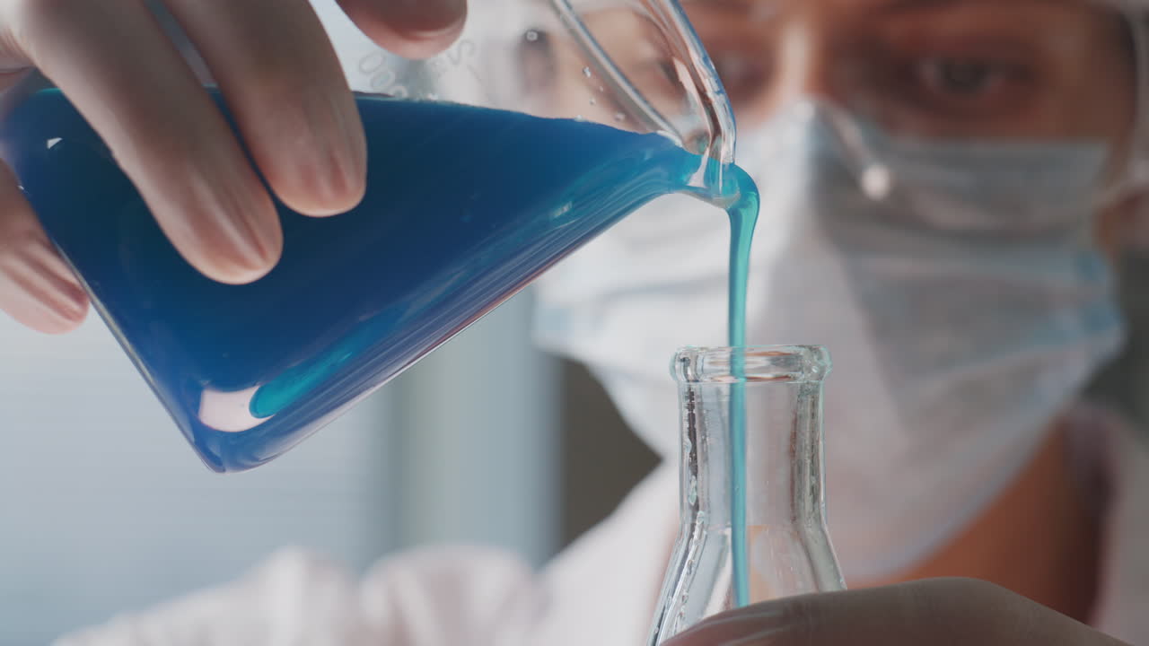 Scientist Pouring Blue Liquid from Beaker into Flask during Lab Work