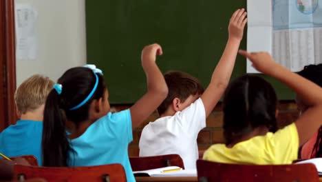 Young-pupils-raising-hands-during-lesson-in-classroom