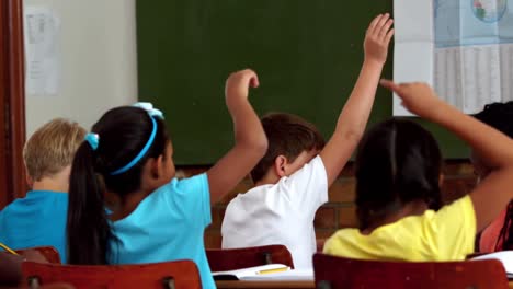 alumnos jóvenes levantando las manos durante la lección en el aula
