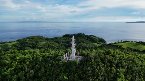 la vista aérea se aleja del faro de bote en lo alto de una colina cubierta de árboles en catanduanes, filipinas, revelando toda la isla y el océano