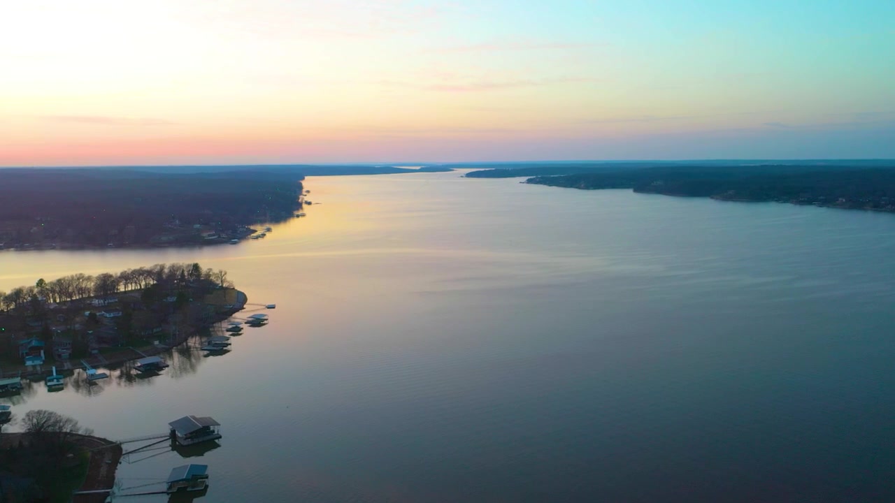 Paesaggio aereo panoramico del lago Bull Shoals con acqua calma del bacino idrico, costa boscosa degli Ozark, case sul lago, moli coperti e cielo serale colorato, ideale per riprese di viaggio o vacanza.