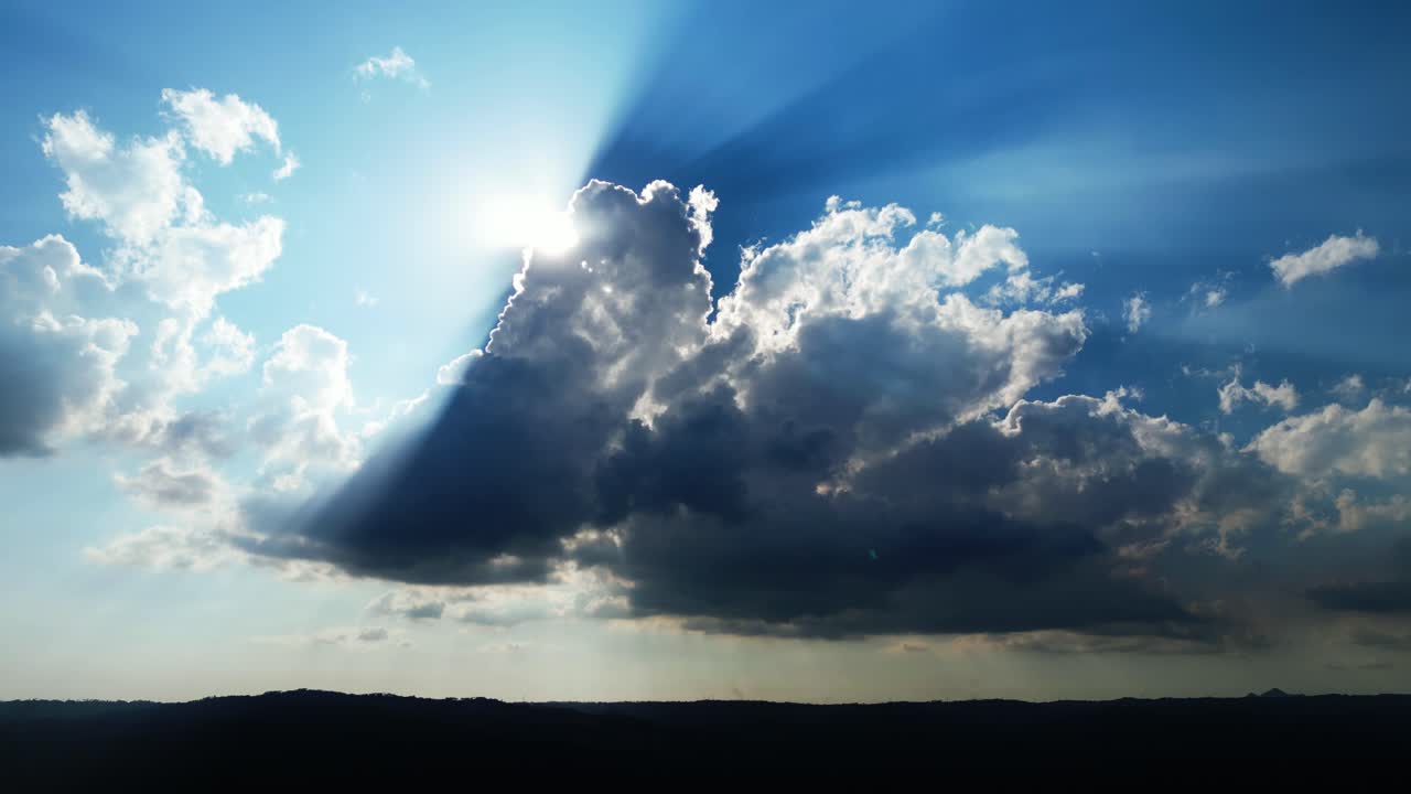 Formazioni nuvolose a lento movimento con la luce solare radiosa che filtra attraverso un cielo blu dalle texture evidenti durante il giorno.