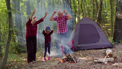 Ältere-Großmutter-Und-Großvater-Mit-Enkelin-Tanzen-Und-Feiern-Am-Lagerfeuer-Im-Wald.