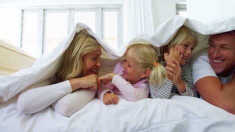 familia feliz acostada bajo una manta en la cama 4k