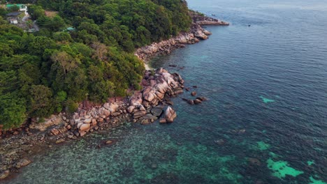 Capturing-the-beauty-of-a-tropical-island,-turquoise-waters-and-rocky-coastline,-this-aerial-view-shows-vibrant-blue-and-green-hues-against-rugged-cliffs-and-shores