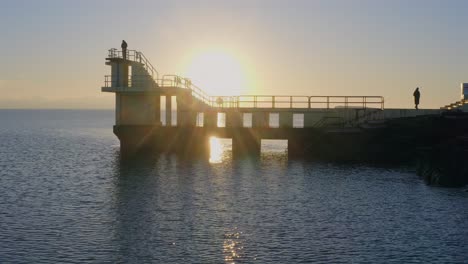 aerial drone footage gliding over the galway coast with a backlit diving board at sunset.