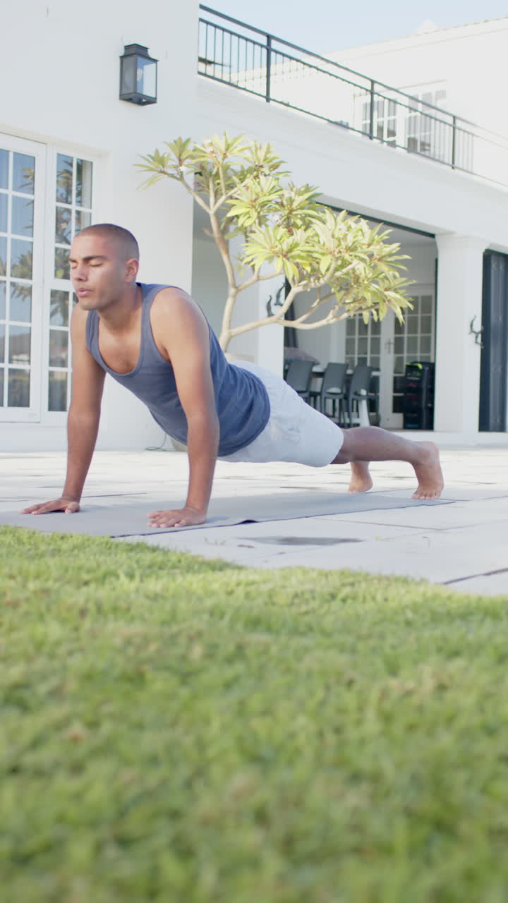 Vertical video of focused anglo indianl man practicing yoga in sunny garden, slow motion