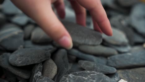 female hand picking up flat rock on beach, slow motion close up