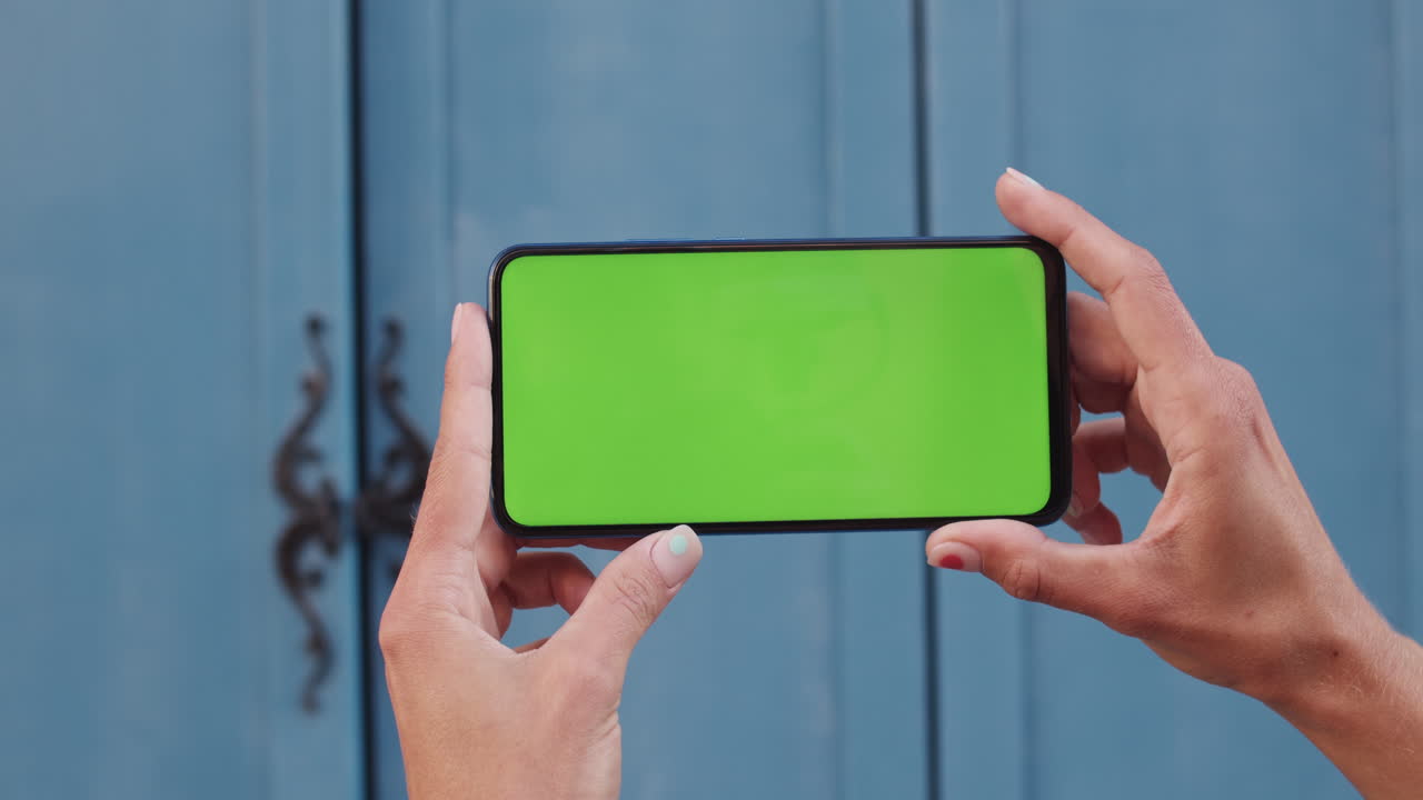 Hands holding a smartphone with a green screen against a blue background