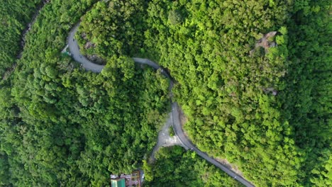 Vista-Aérea-De-Una-Estrecha-Y-Sinuosa-Carretera-De-Montaña-Rodeada-De-Una-Exuberante-Naturaleza-Verde