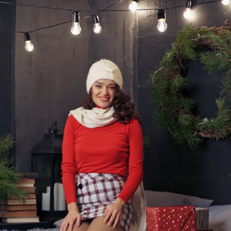 lady putting on white knitted hat. beautiful woman poses to the camera in room decorated before winter holidays. fest spirit