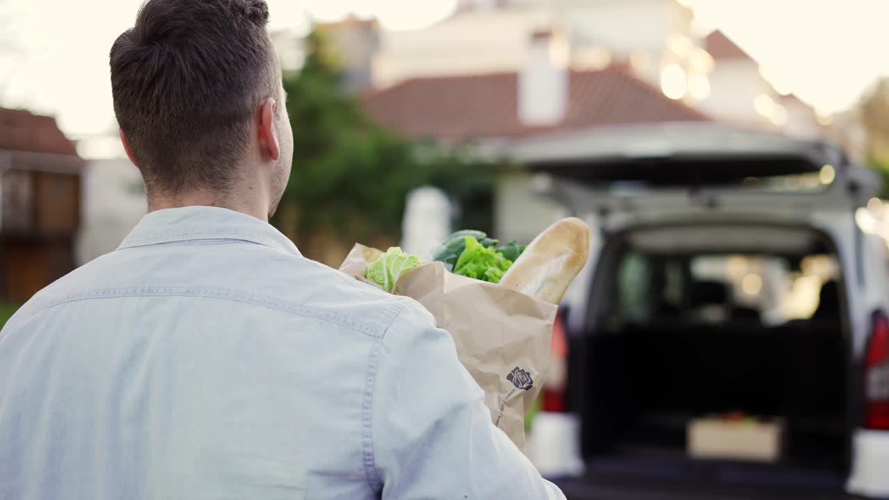 hombre guapo irreconocible yendo al coche llevando una bolsa de papel con comestibles al aire libre