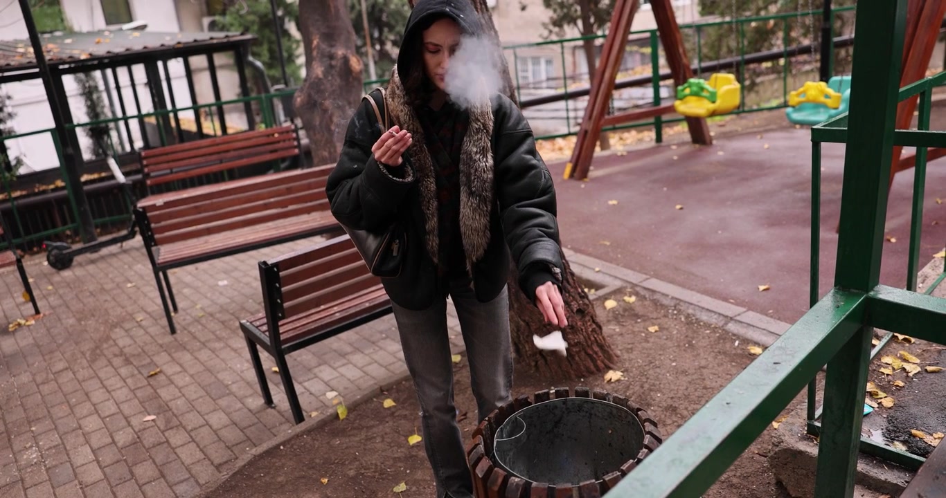 Ung kvinde ryger cigaret nær legeplads og smider affald