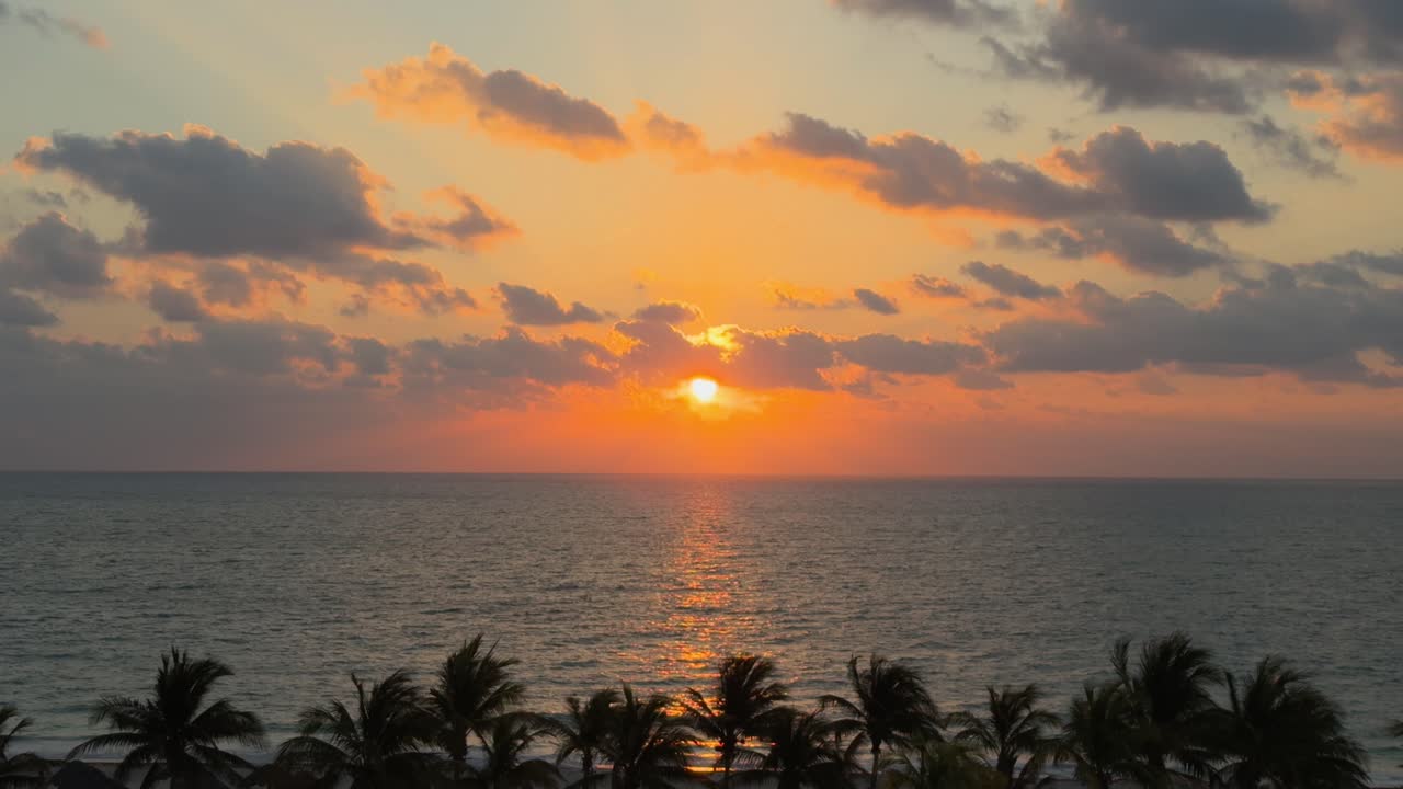 Golden sun behind clouds during Caribbean sunrise with sea and palm trees