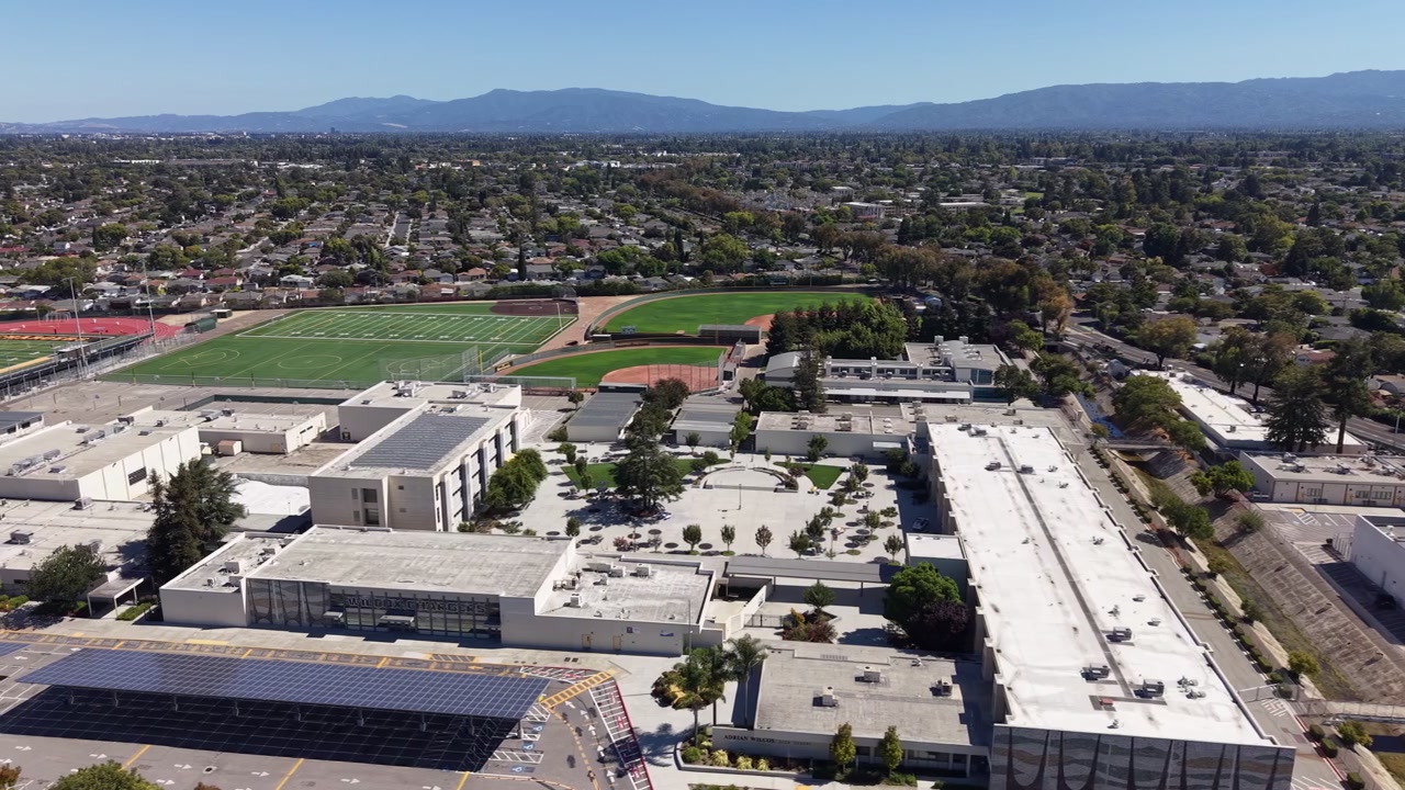 Aerial perspective of the Adrian Wilcox high school campus, featuring modern buildings, sports fields, and solar panels, set against the suburban landscape of Santa Clara, California
