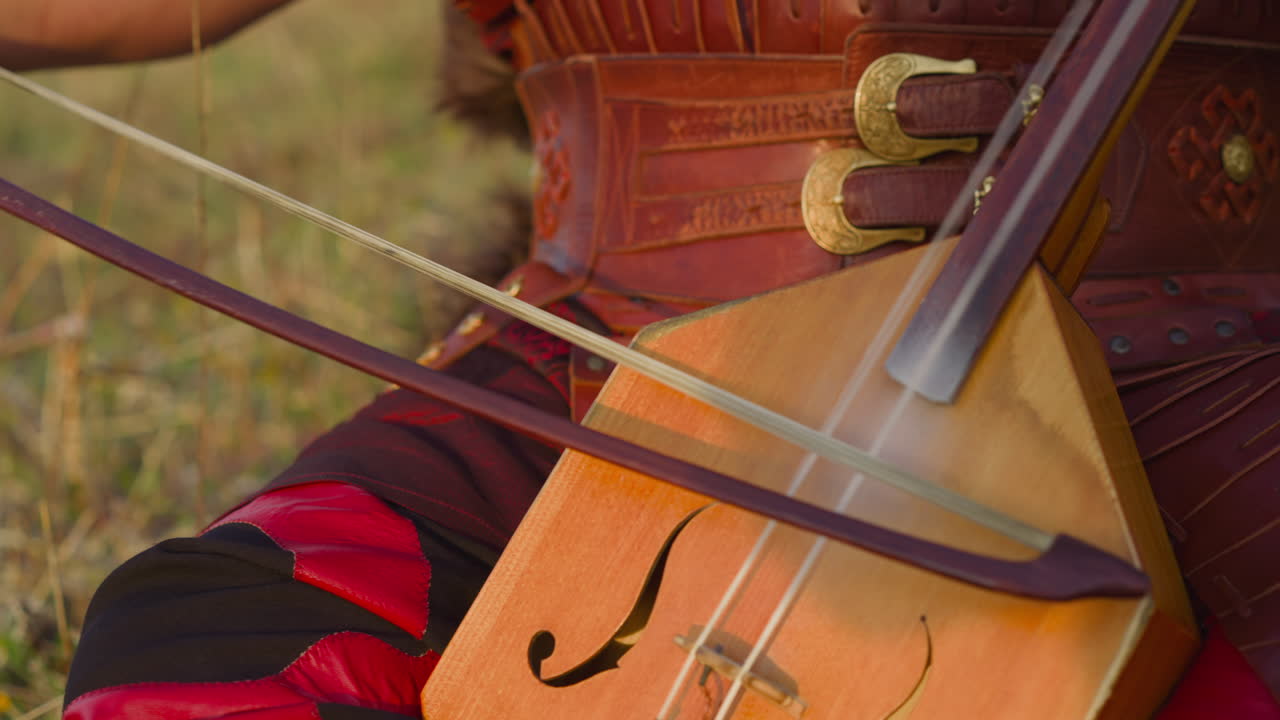 Musician in ethnic leather clothes plays igil on field