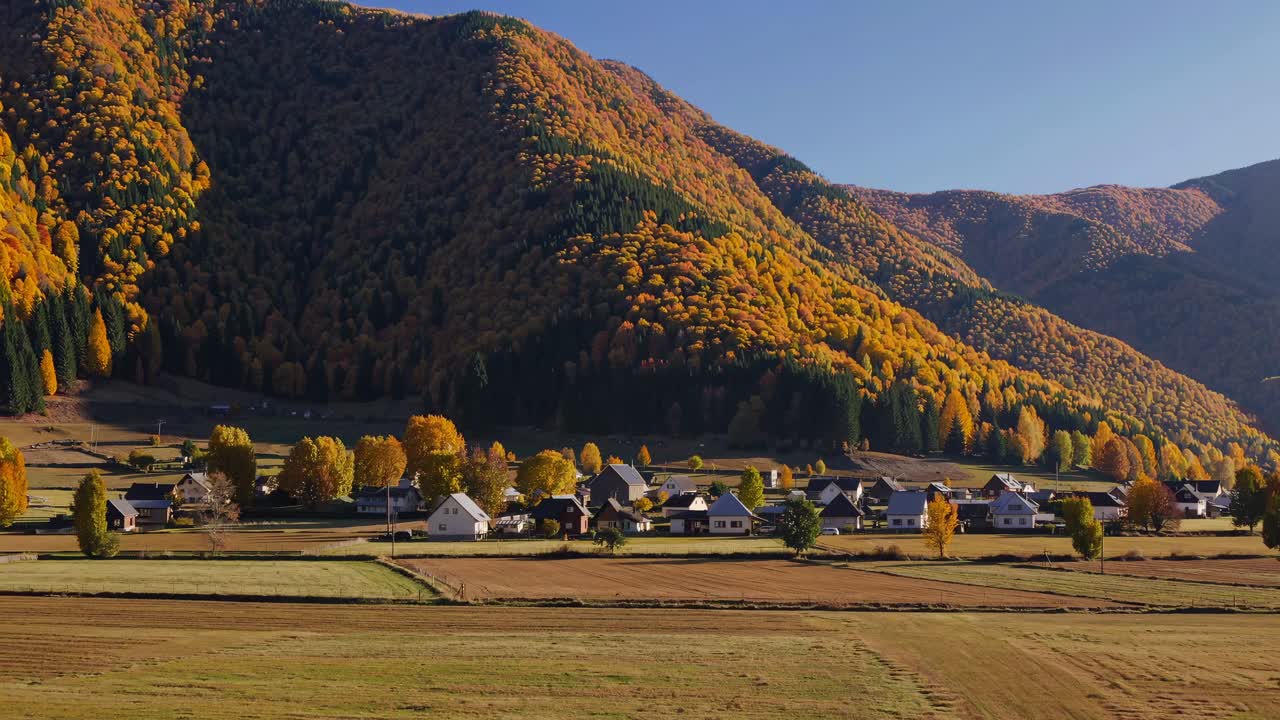 Aerial video view of a village nestled in a valley with vibrant autumn foliage on surrounding hills