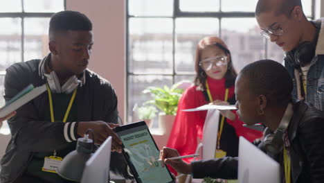 Jóvenes-Empresarios-Se-Reúnen-Con-Una-Mujer-Líder-Del-Equipo-Afroamericano-Que-Usa-Una-Tableta-Que-Muestra-Datos-De-Marketing-En-La-Estrategia-De-Compartir-Pantalla,-Colegas-Que-Colaboran-En-Una-Sesión-Informativa-En-La-Oficina